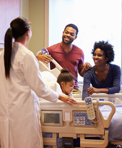 A photo of a child in hospital bed and her parents talking to the doctor in the room