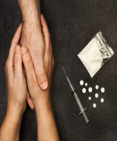 A photo of hands in hands and opioid pills and syringe near them trying to indicate the role of social support in  addresing opioid crisis