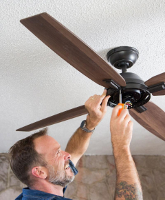 A white middle aged man wih tatto on his hand and a smile on his face is fixing a fan